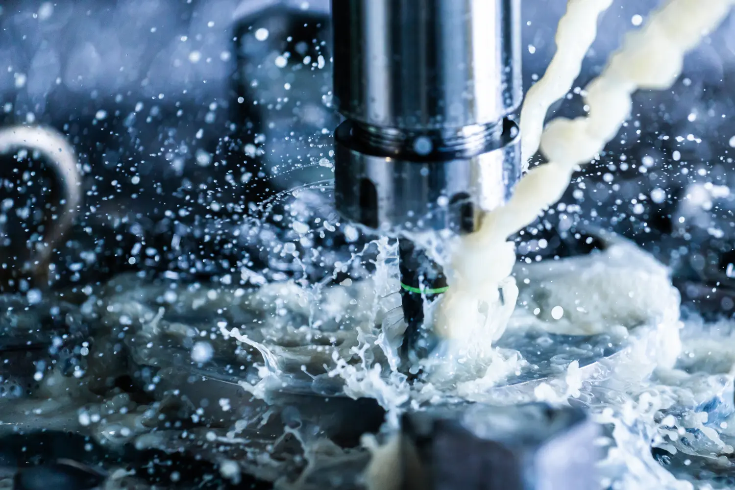 Nahaufnahme eines vertikalen CNC-Stahlfräsprozesses mit externen Kühlmittelströmen, Spritzern und einer Menge Metallspäne, hoher Kontrast